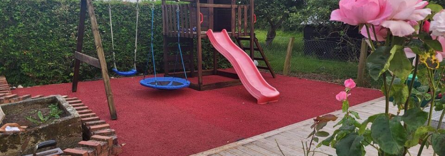 Red wet pour, to soften landings, underneath a children's climbing frame